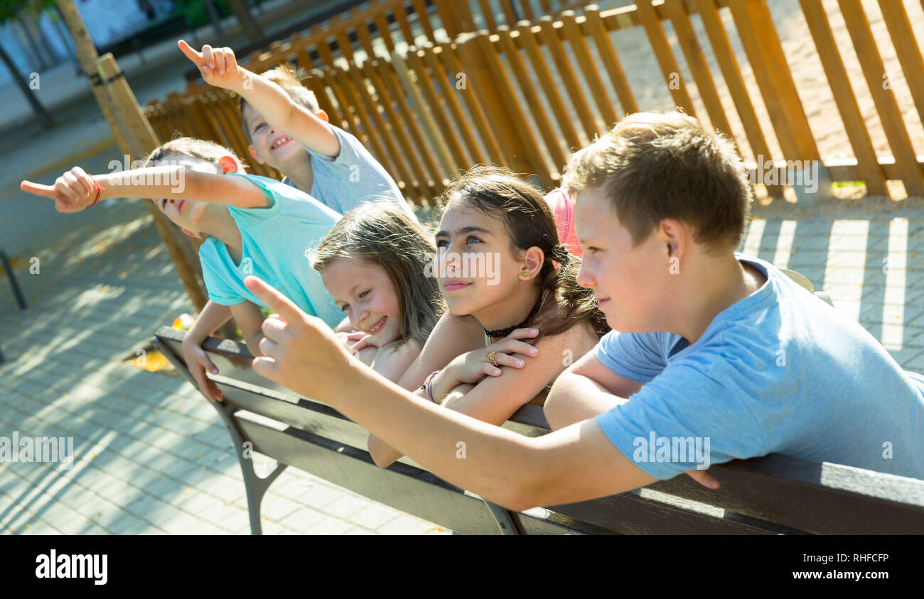 Five children sitting on a bench at the playground and point to ...