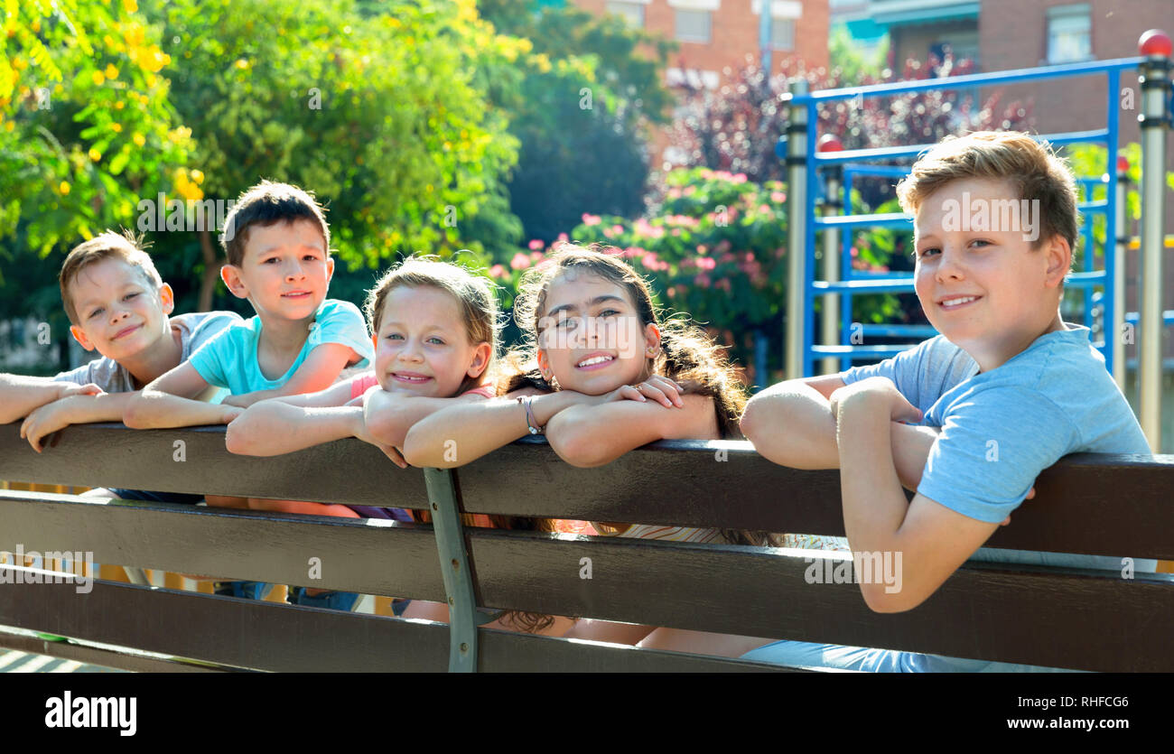 Five glad positive smiling children sitting on a bench at the ...