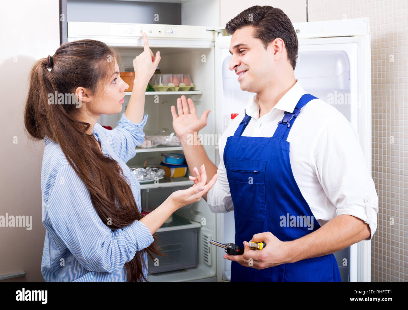 Young  housewife and happy handyman with tooling standing near fridge indoors Stock Photo