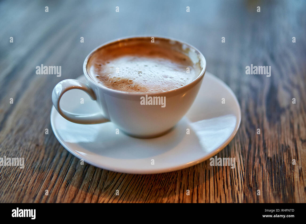 Hot Cappuccino In White Cup On Wooden Table placed centrally Stock Photo