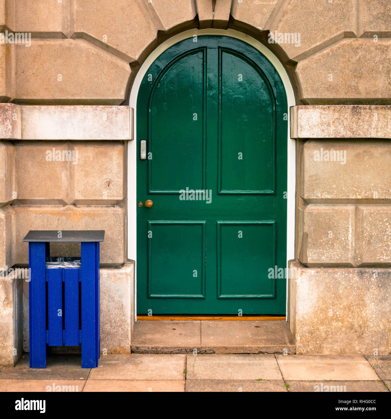 Solid Traditional Wooden Green Painted Door With A Blue Waste Bin Stock Photo