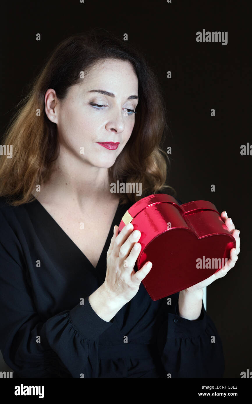 Portrait of a mature woman in her 40s looking expectantly the box of her present, expectant glance, curiosity. Stock Photo