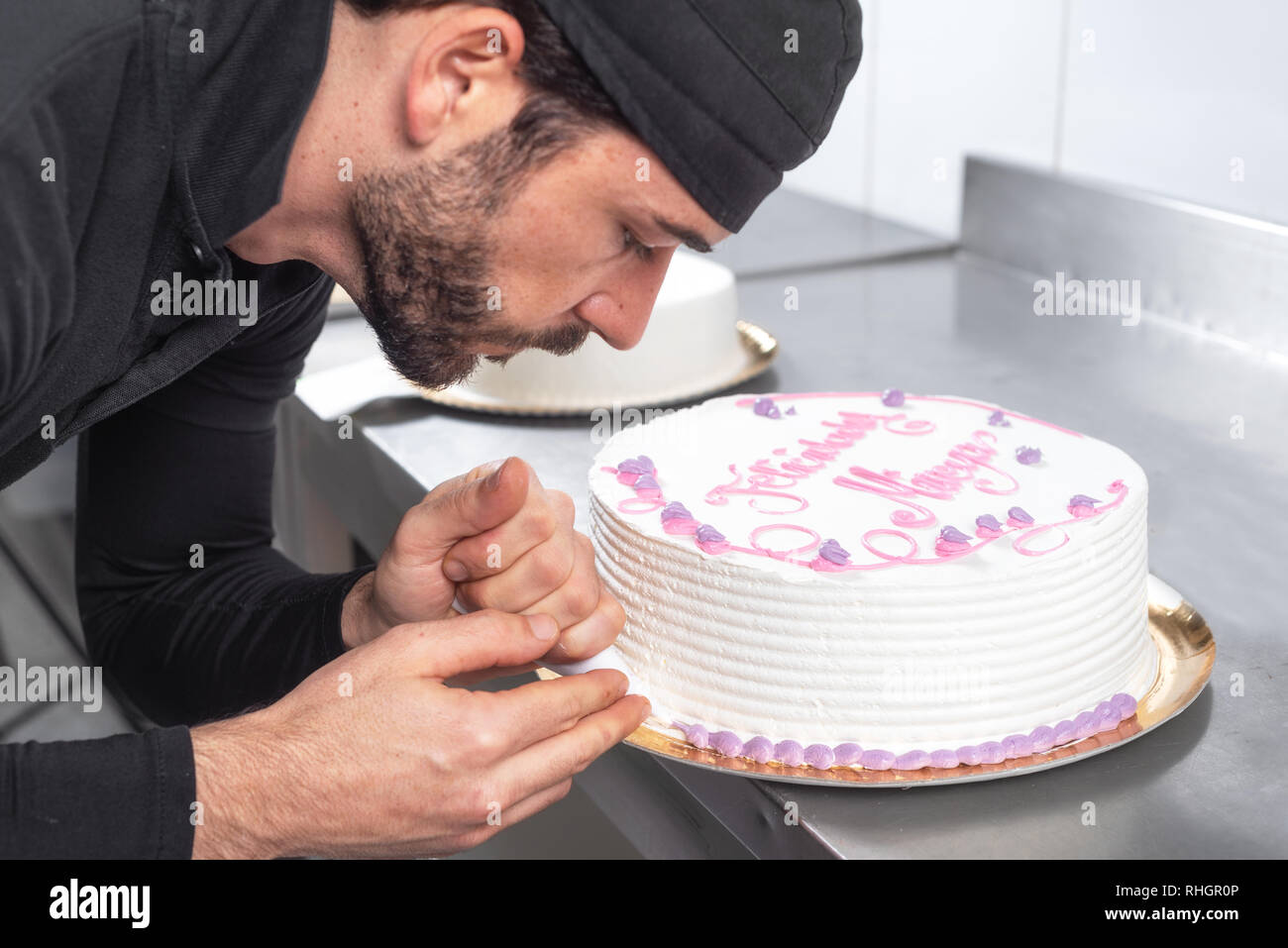 Handsome professional confectioner making a delicious cake in the pastry shop . Stock Photo