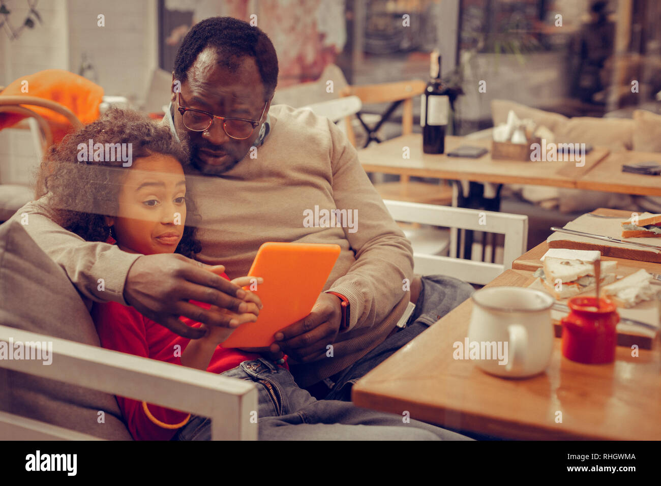 Dark-eyed girl feeling bored while watching film on tablet with father Stock Photo