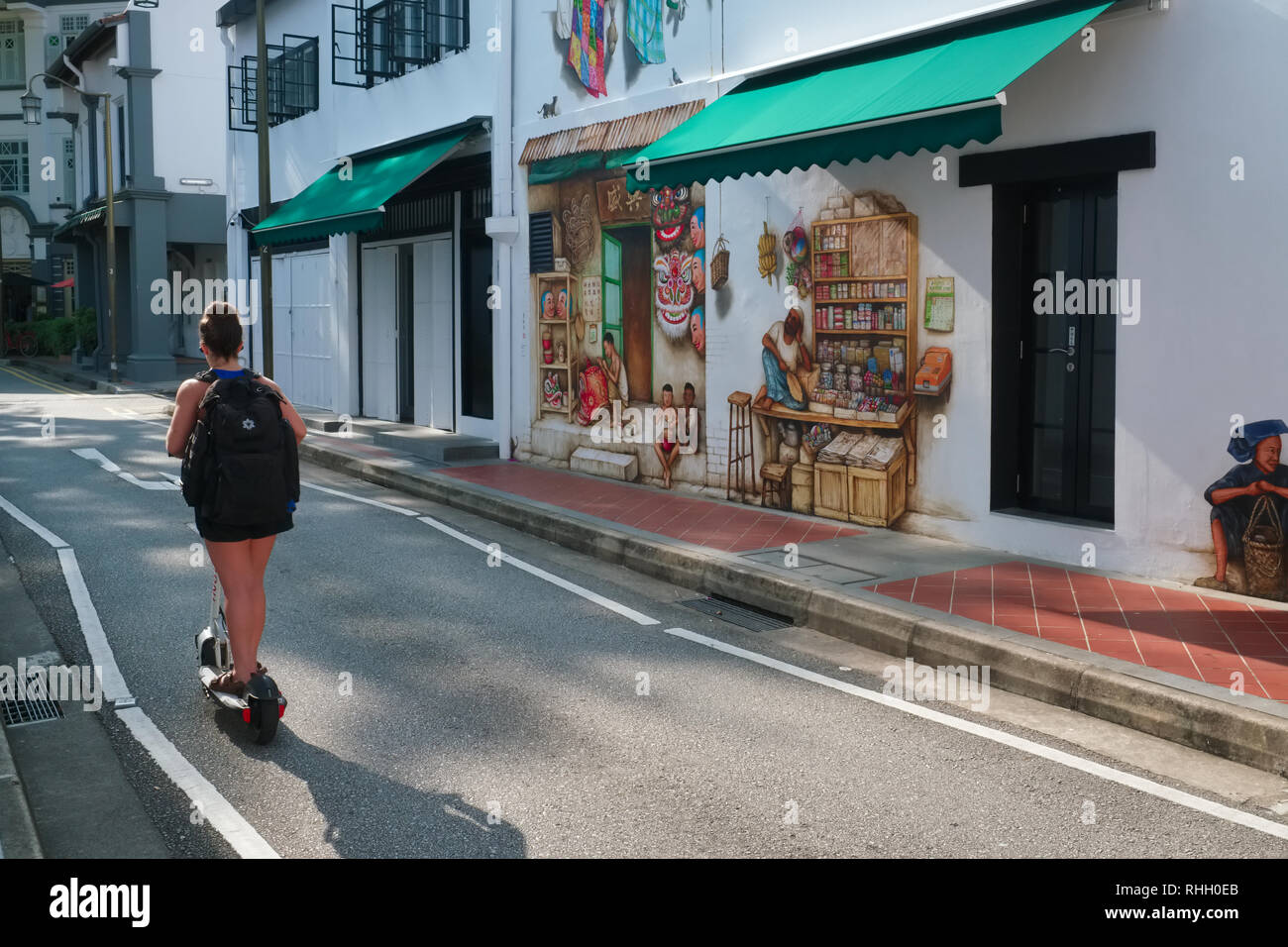 A Western tourist on a electric scooter passes some wall paintings in