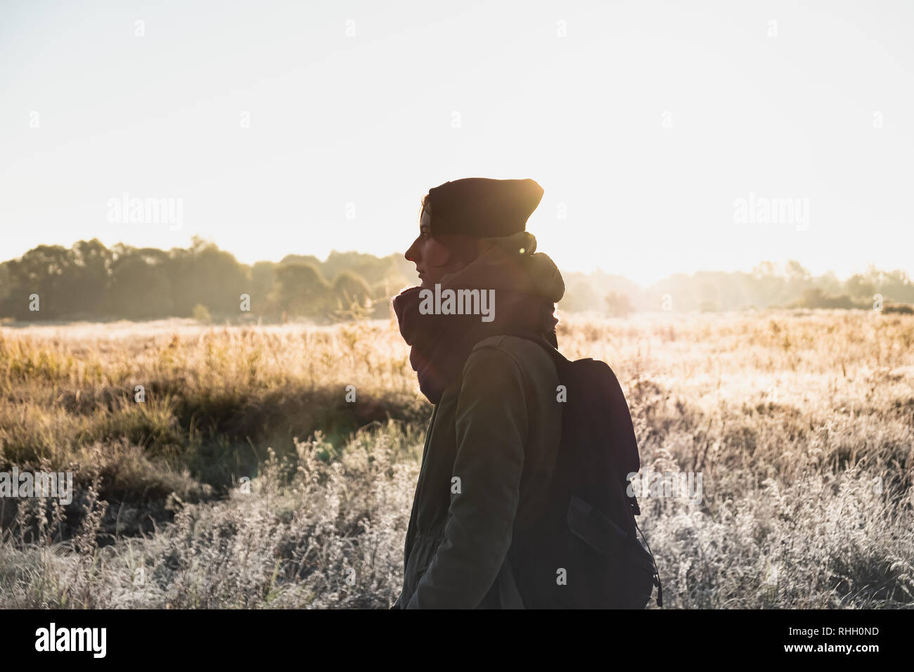 Backlit portrait of beautiful woman in direct sunlight. Female person walking outdoors on chilly sunny morning in autumn Stock Photo