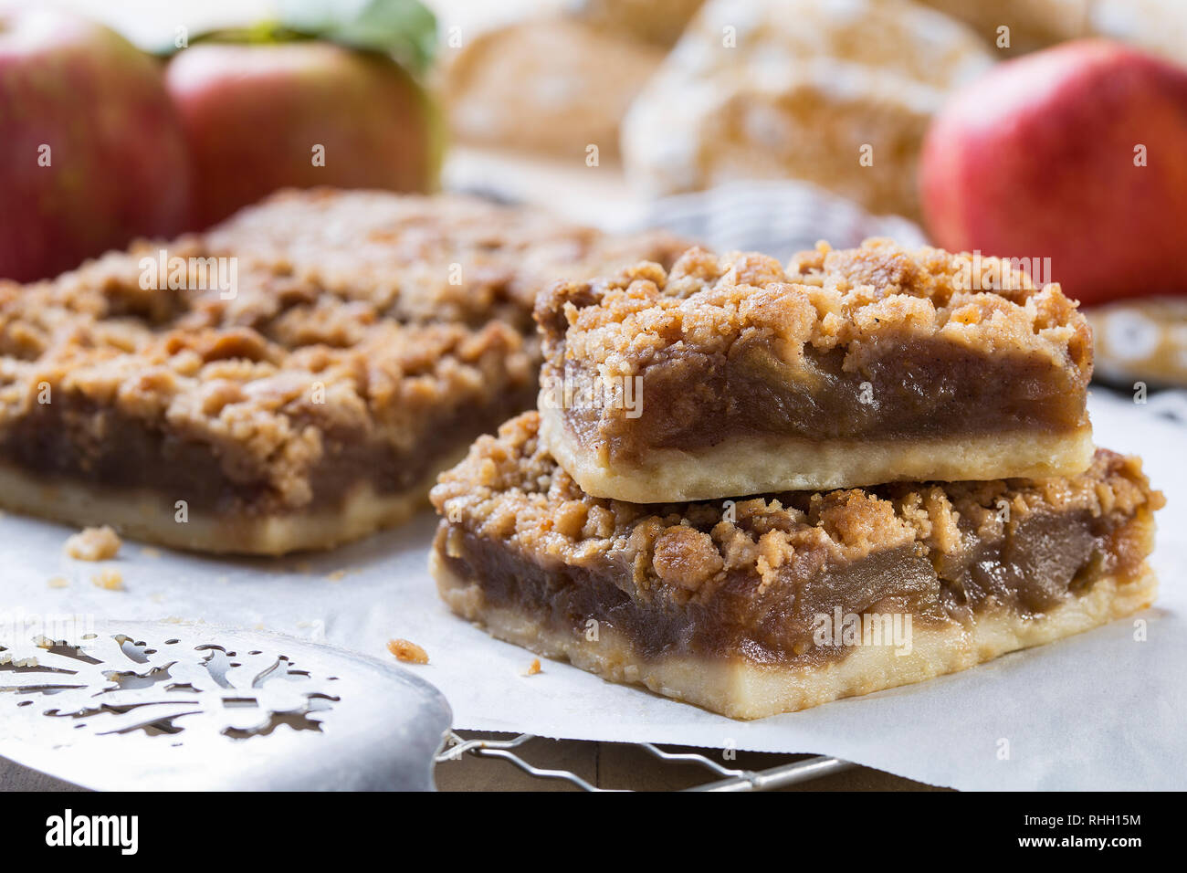 baked apple bars on cooling rack with antique spatula, parchment paper, apples, and towel Stock Photo