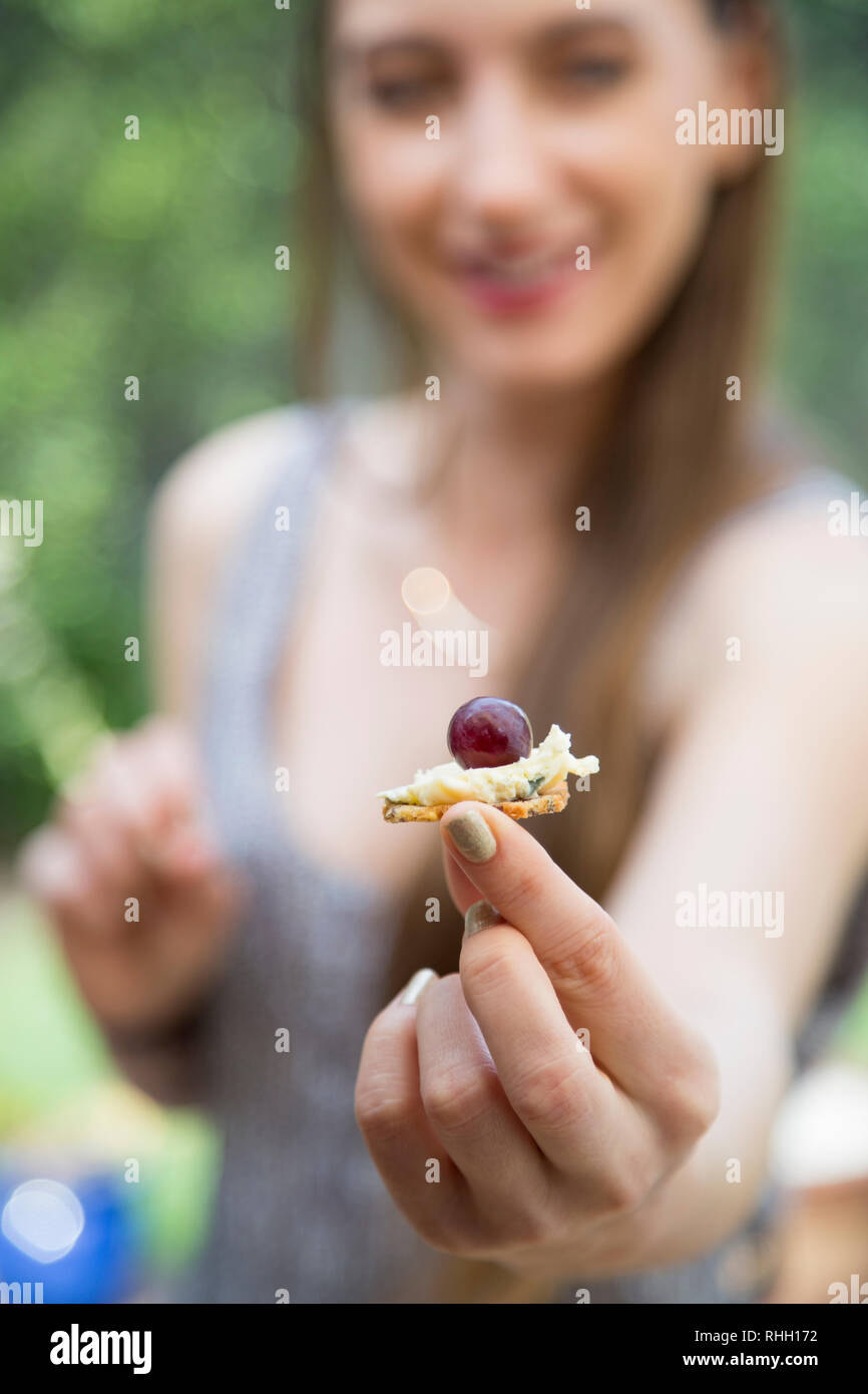 Hand holding appetizer bite with grape, cheese, and cracker, female out of focus in background. Stock Photo