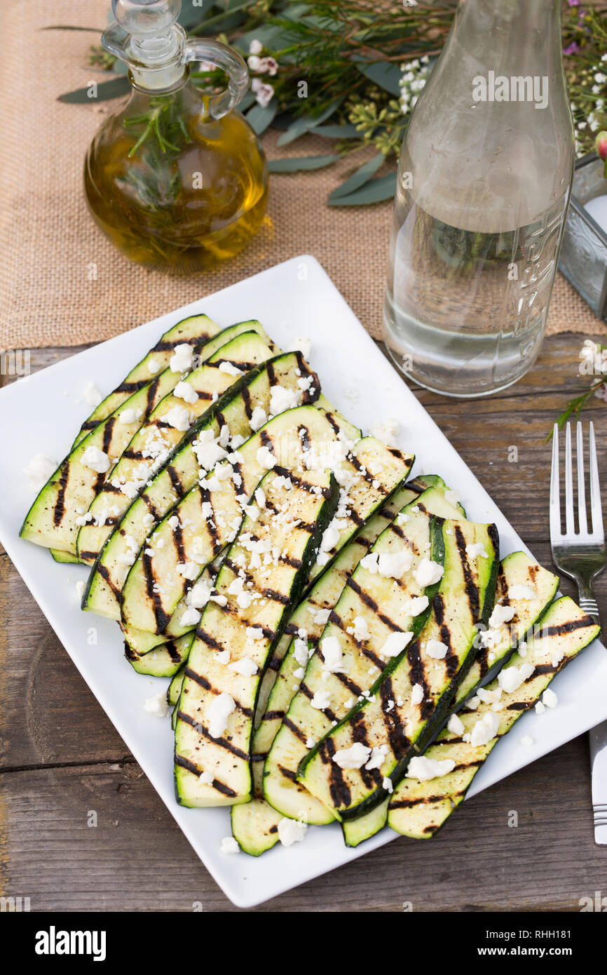 White rectangular serving platter of grilled zucchini on wooden table for outdoor backyard dinner party. Stock Photo