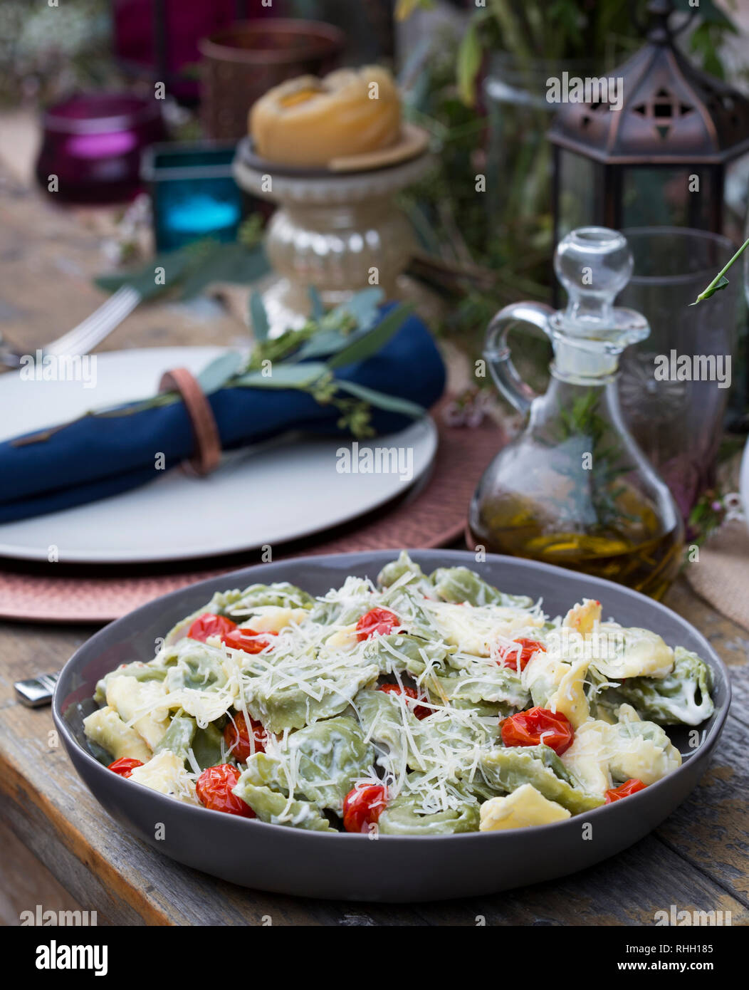 Serving bowl of green and yellow ravioli with tomatoes and shredded parmesan cheese on wooden table for backyard outdoor dinner party, with olive oil. Stock Photo