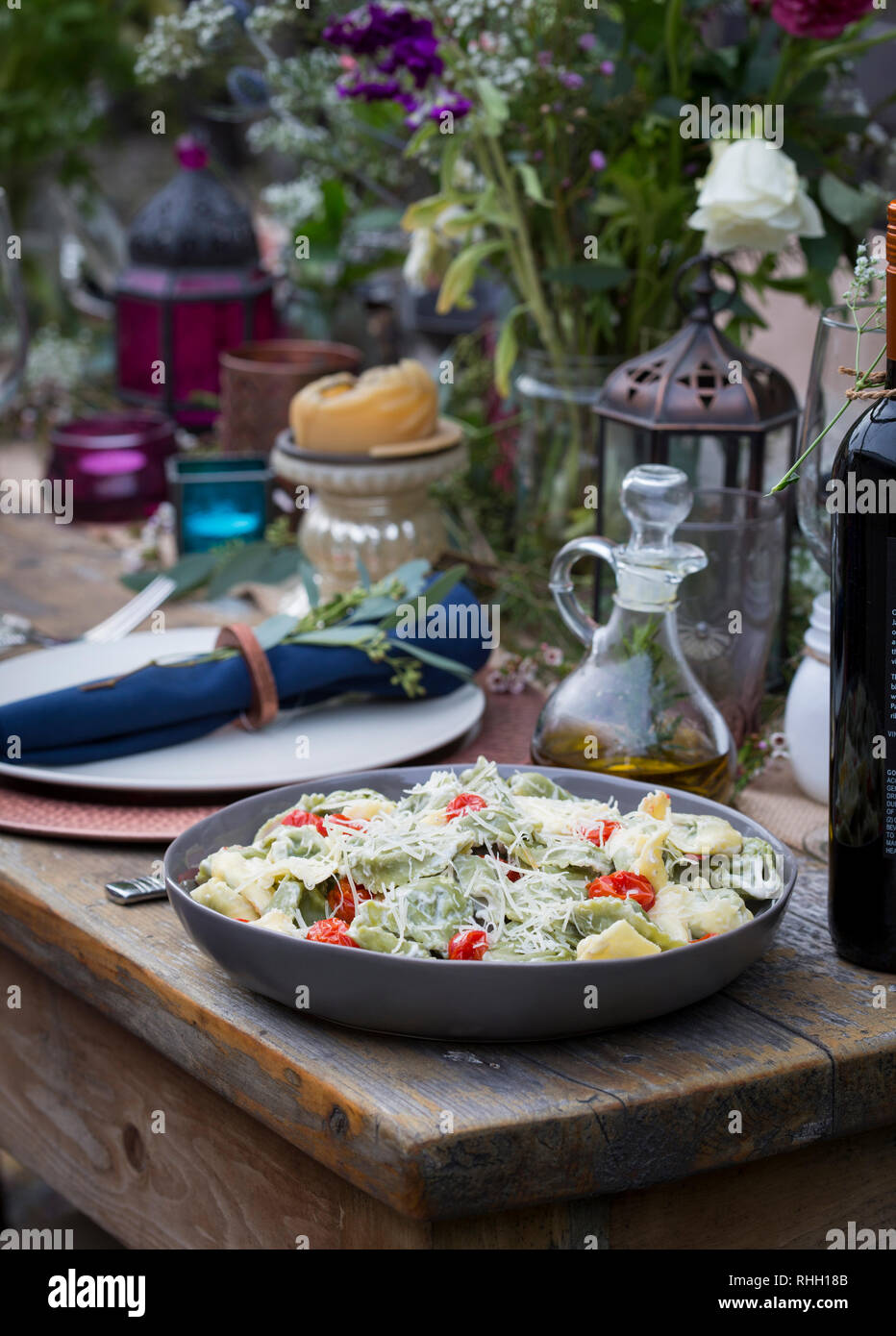 Serving bowl of green and yellow ravioli with tomatoes and shredded parmesan cheese on wooden table for backyard outdoor dinner party, with olive oil. Stock Photo