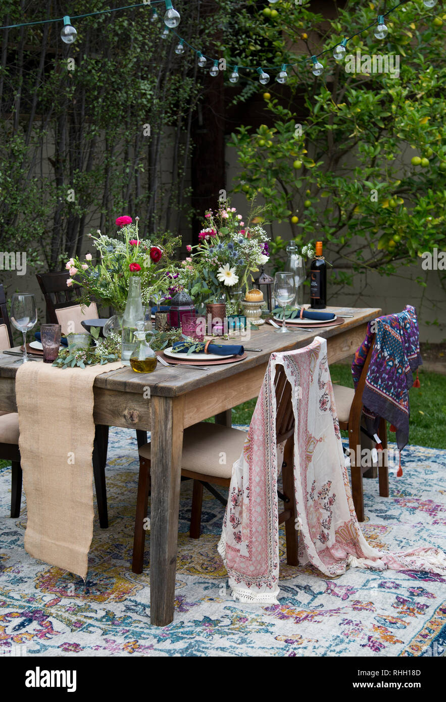 Outdoor backyard dinner party table setting with flowers, place settings, string lights and fabric. Stock Photo