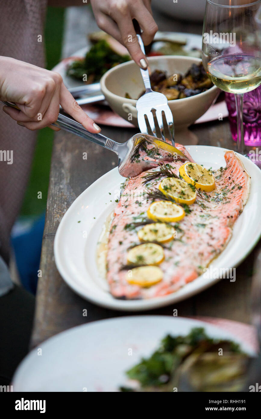 Hands serving salmon with lemon with silver fork from platter. Stock Photo