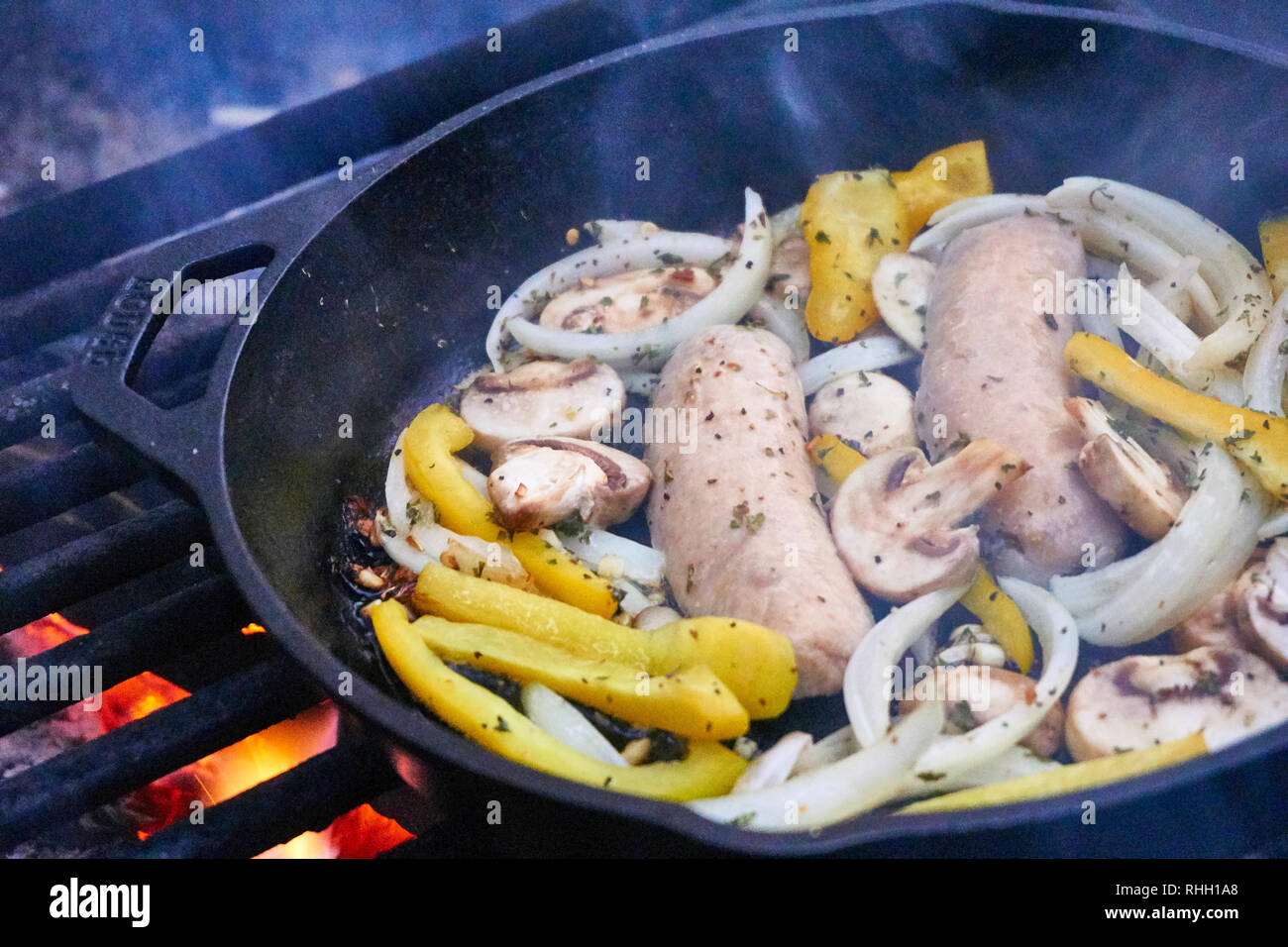 https://c8.alamy.com/comp/RHH1A8/cast-iron-skillet-camping-meal-over-campfire-grill-flames-with-sausage-peppers-mushrooms-and-onions-RHH1A8.jpg