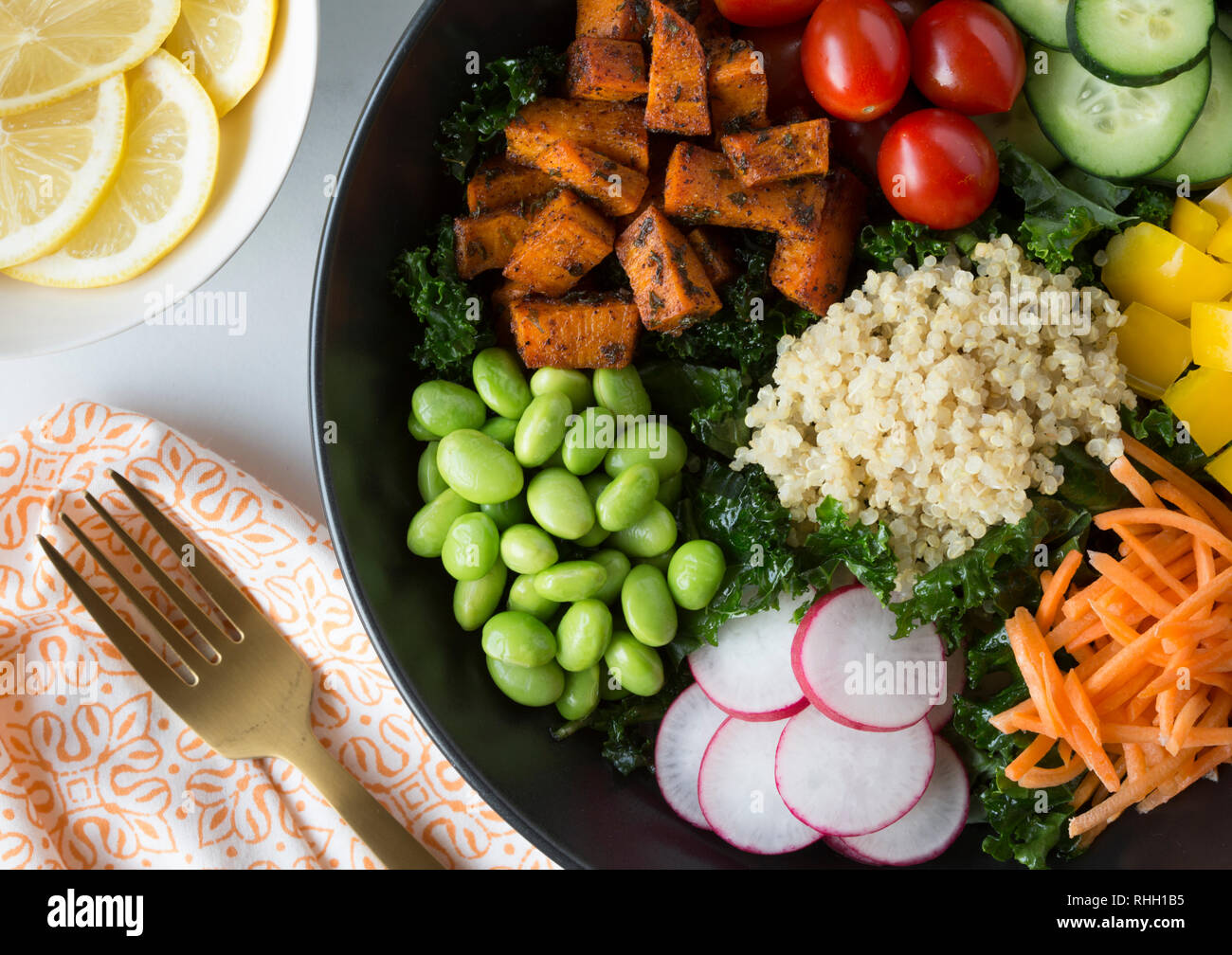 Aerial view of healthy kale salad bowl with vegetables- sweet potatoes, tomatoes, cucumber, bell peppers, carrot, radish, and edamame with quinoa. Stock Photo