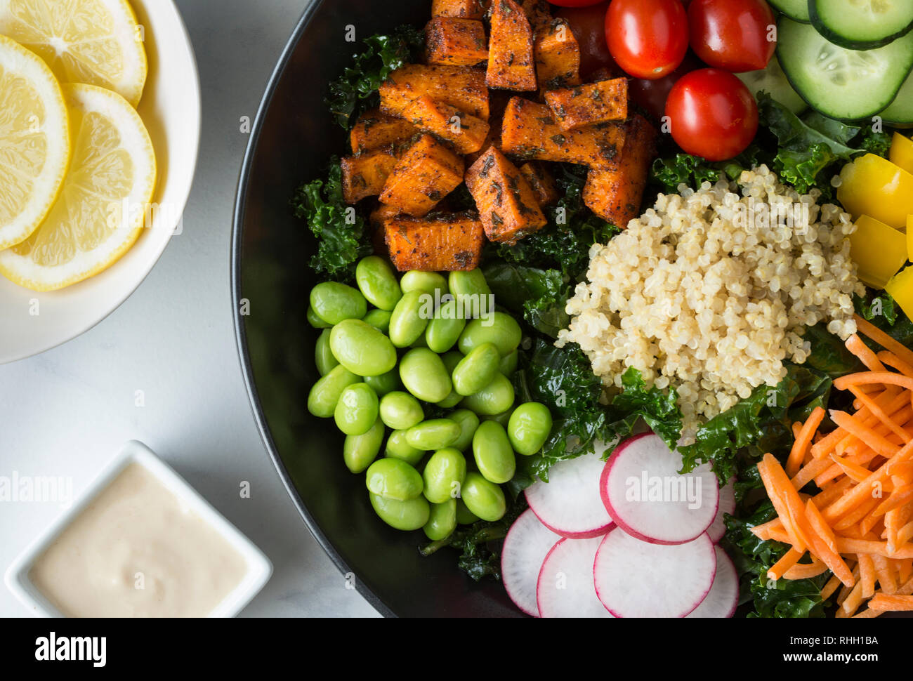 Aerial view of healthy kale salad bowl with vegetables- sweet potatoes, tomatoes, cucumber, bell peppers, carrot, radish, and edamame with quinoa. Stock Photo