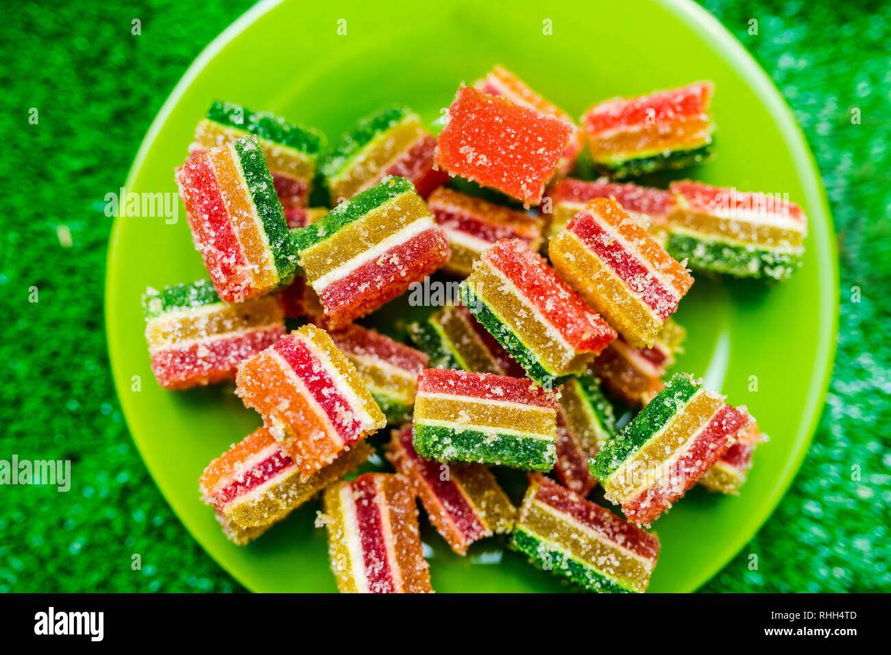 Colorful sugarcoated fruit jelly candy on a green plate. Close up over