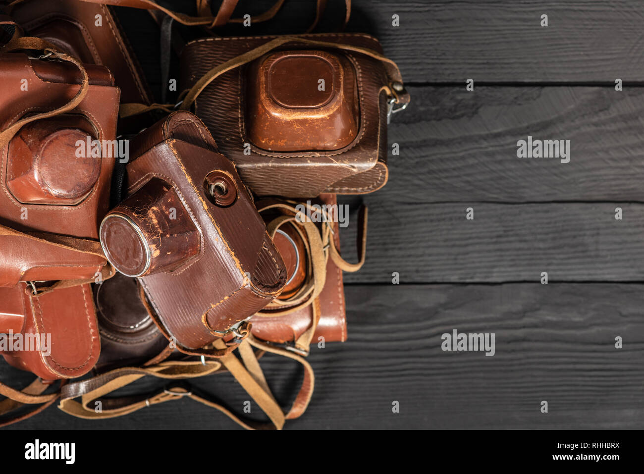 Heap of 35mm retro cameras in leather covers on black, top view. Collection of old things and antiques, auctions Stock Photo