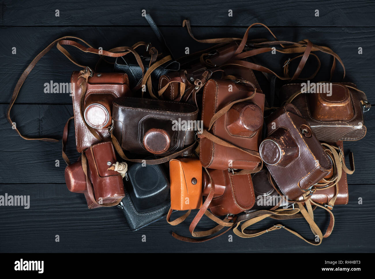 Heap of 35mm retro cameras in leather covers on black, top view. Collection of old things and antiques, auctions Stock Photo