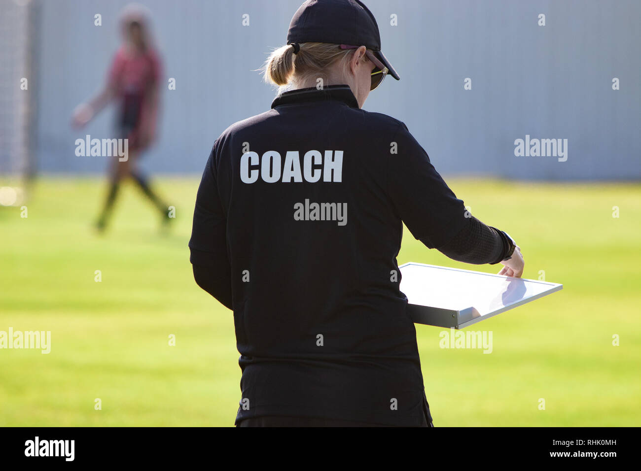 Back view of female sport coach in black COACH shirt at an outdoor sport field, looking at her game plan chart, good for sport or coaching concept Stock Photo