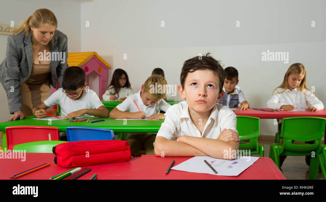 Portrait of bored schoolboy sitting in classroom with classmates and ...