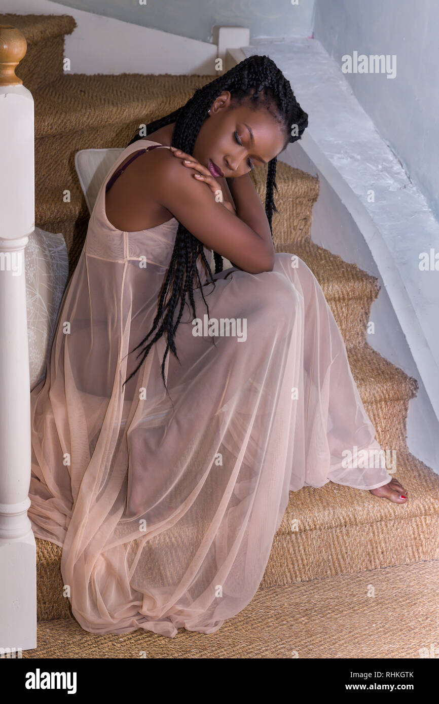 Pretty young woman in sheer nightgown sitting on stairs Stock
