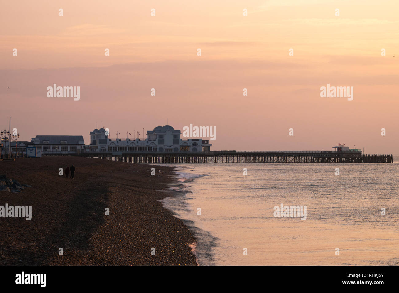 a couple waking along the pebble beach at Southsea seafront during sunset with south parade pier in the background Stock Photo