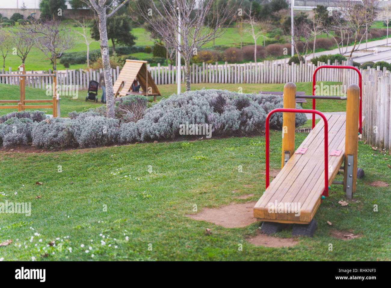 Seesaw, Red wooden kids playground equipment in a park with green grass, bushes, trees, and a wooden fence, Oeiras Portugal Stock Photo