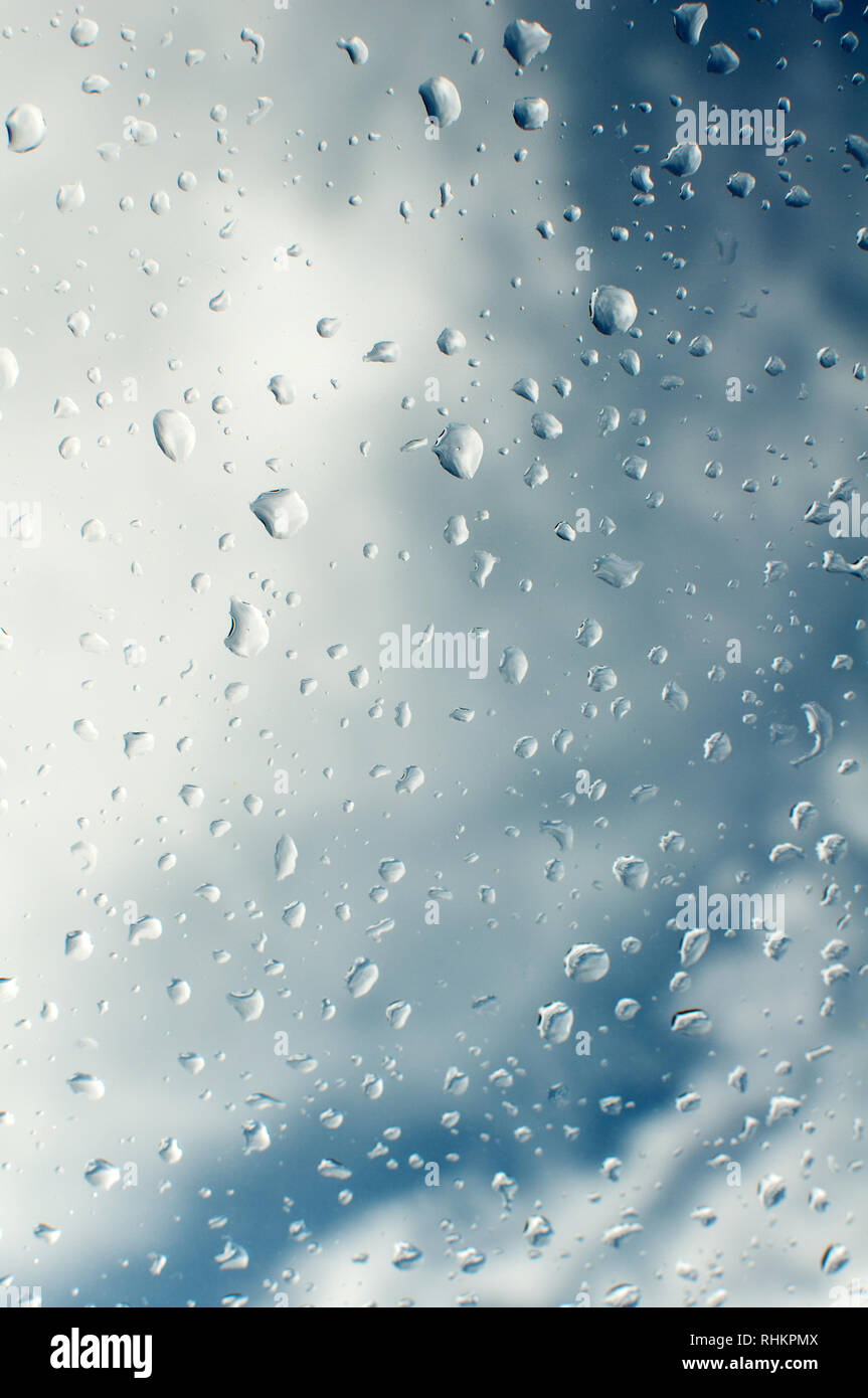 Rain drops on window with blue sky and clouds in the background Stock Photo