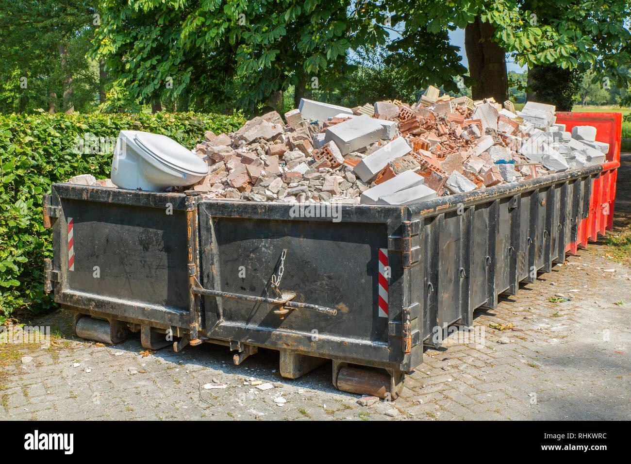 Big metal waste container filled with stones, toilet and other rubble Stock Photo