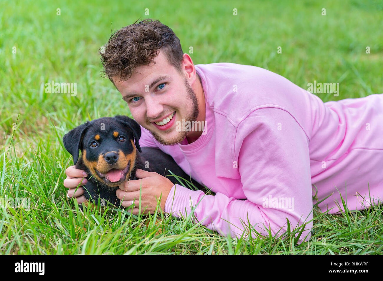 Young caucasian male dog owner   holds lovingly rottweiler puppy in natural meadow Stock Photo