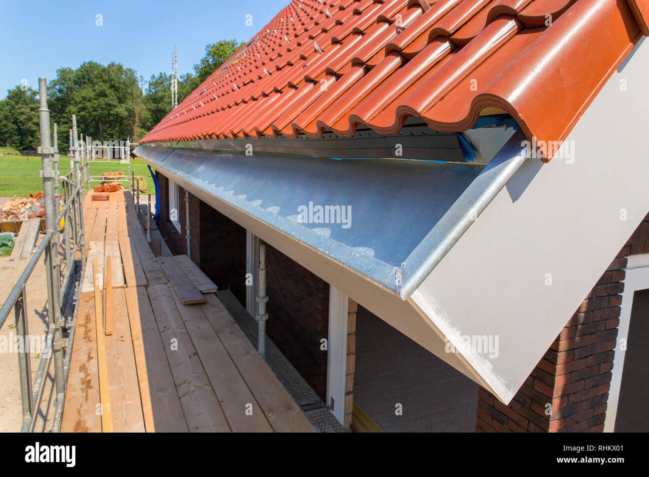Zinc rain gutter with roof tiles and scaffolding at new house Stock Photo