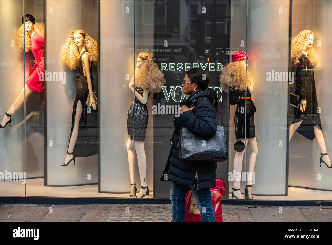 A black lady makes her way past a shop front on London's Oxford Street. The mannequins in the window are all white/caucasian representation Stock Photo