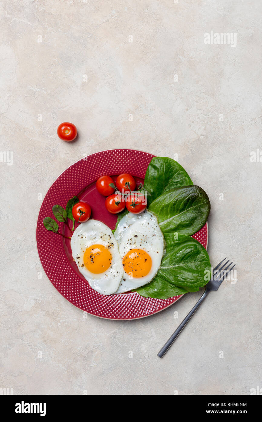 Heart shaped two fried eggs with romano salad and cherry tomatoes at red plate with fork on white background. Vertical concept of healthy food. Free s Stock Photo