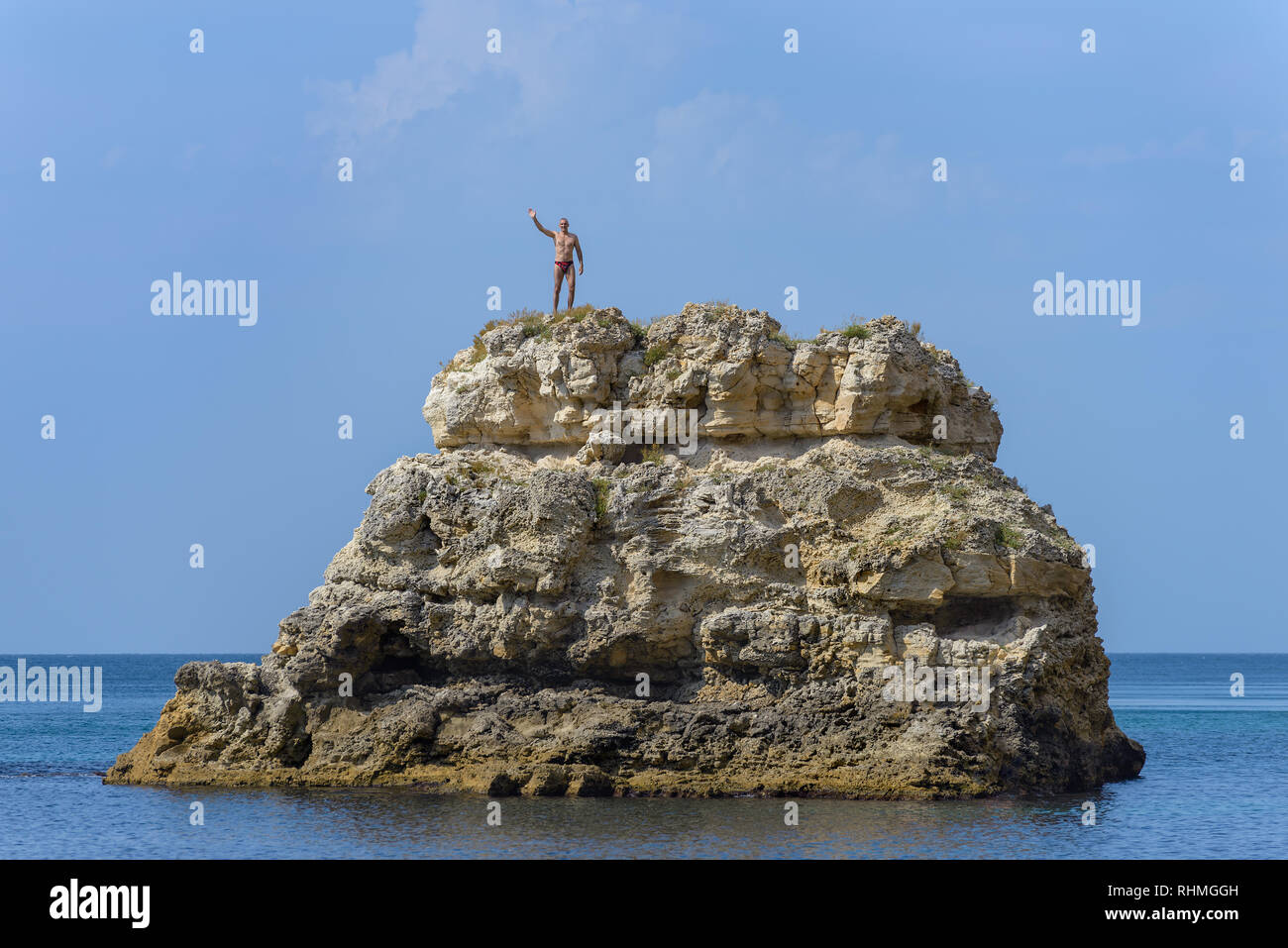 A man in a red swimming trunks stands on top of a cliff Stock Photo