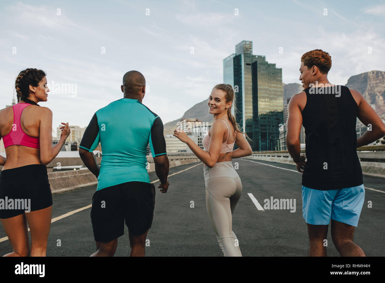 Woman running with her group of runners outdoors. Female exercising with friends outdoors in the city. Girl looking over shoulder while running outdoo Stock Photo