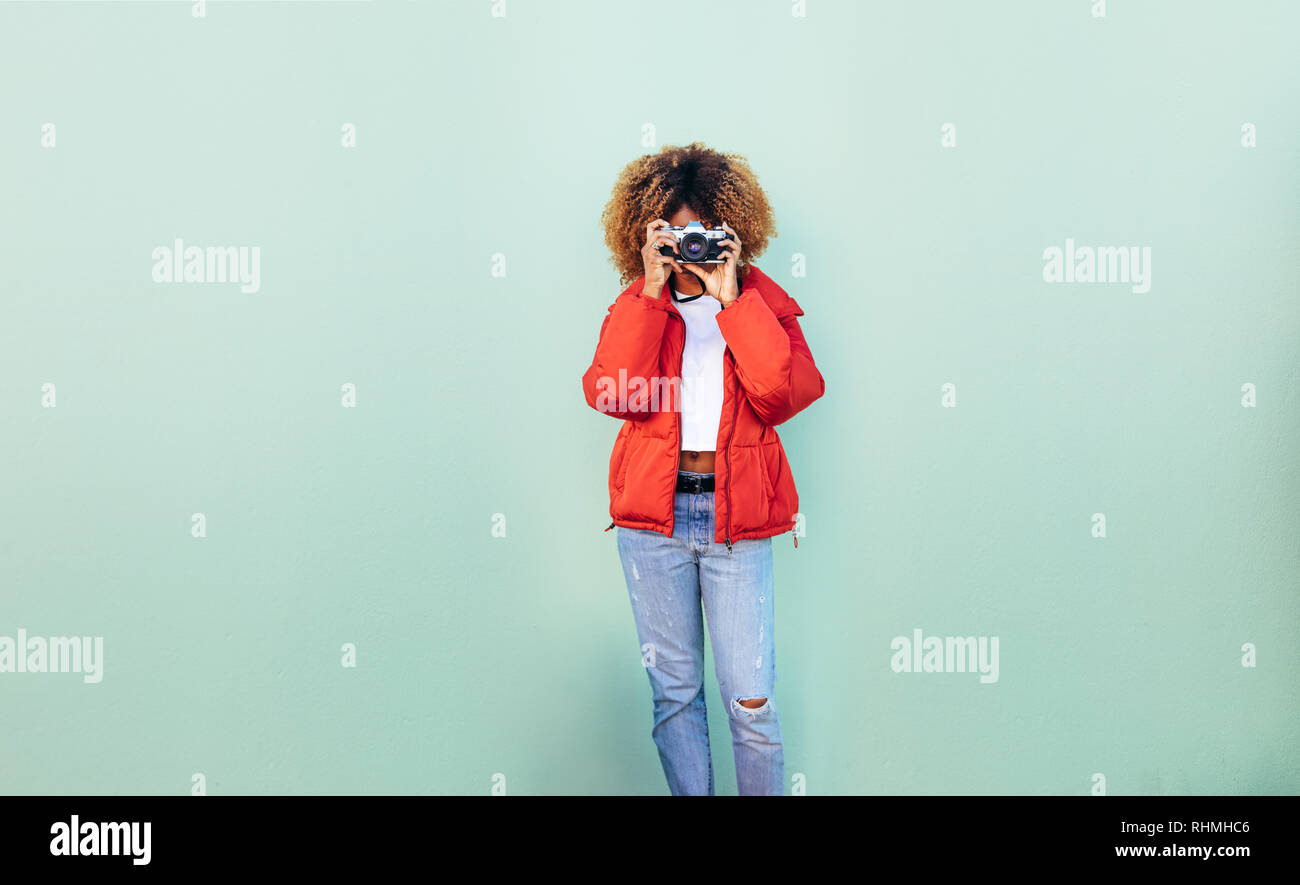Afro american woman shooting a photo looking through a camera. Woman holding a camera to her face taking a photo. Stock Photo