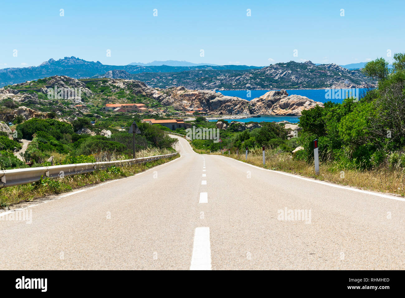 Asphalt empy road surrounded by rocky environment and turquoise sea on the beautiful island of la maddalena, italy Stock Photo