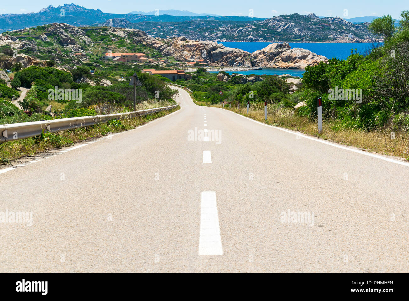 Asphalt empy road surrounded by rocky environment and turquoise sea on the beautiful island of la maddalena, italy Stock Photo