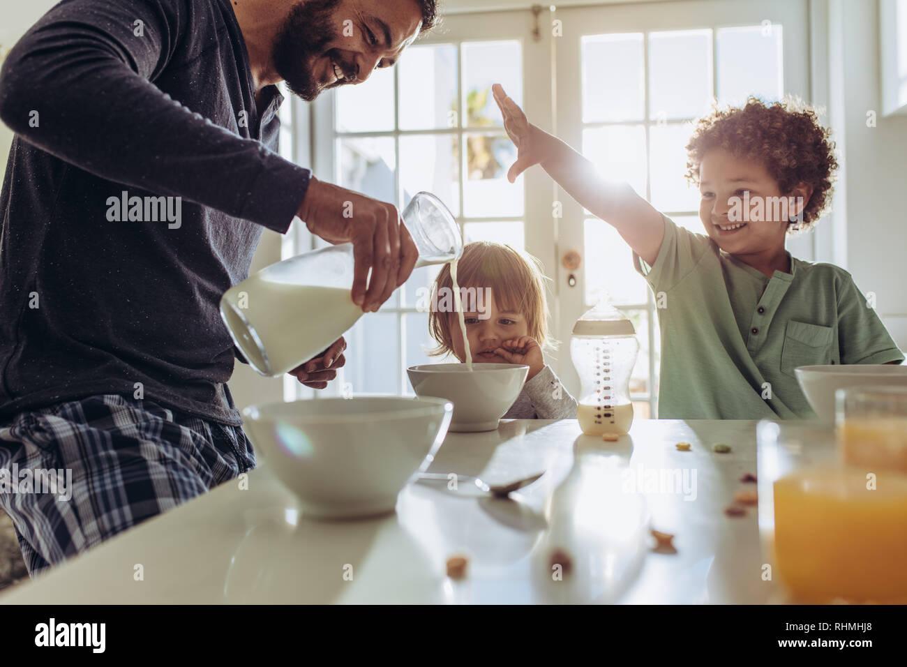 Father making breakfast for his kids at home. Man having fun preparing breakfast at home with his kids. Stock Photo