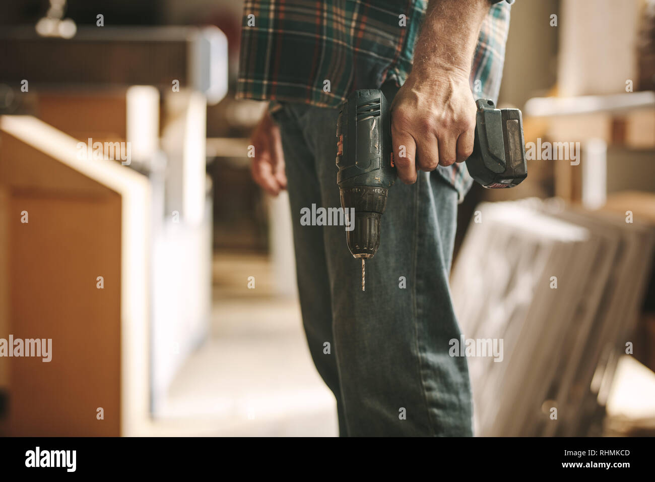 Carpenter holding a hand drill machine at workshop. Cropped shot of man with drilling machine in hand at carpentry workshop. Stock Photo