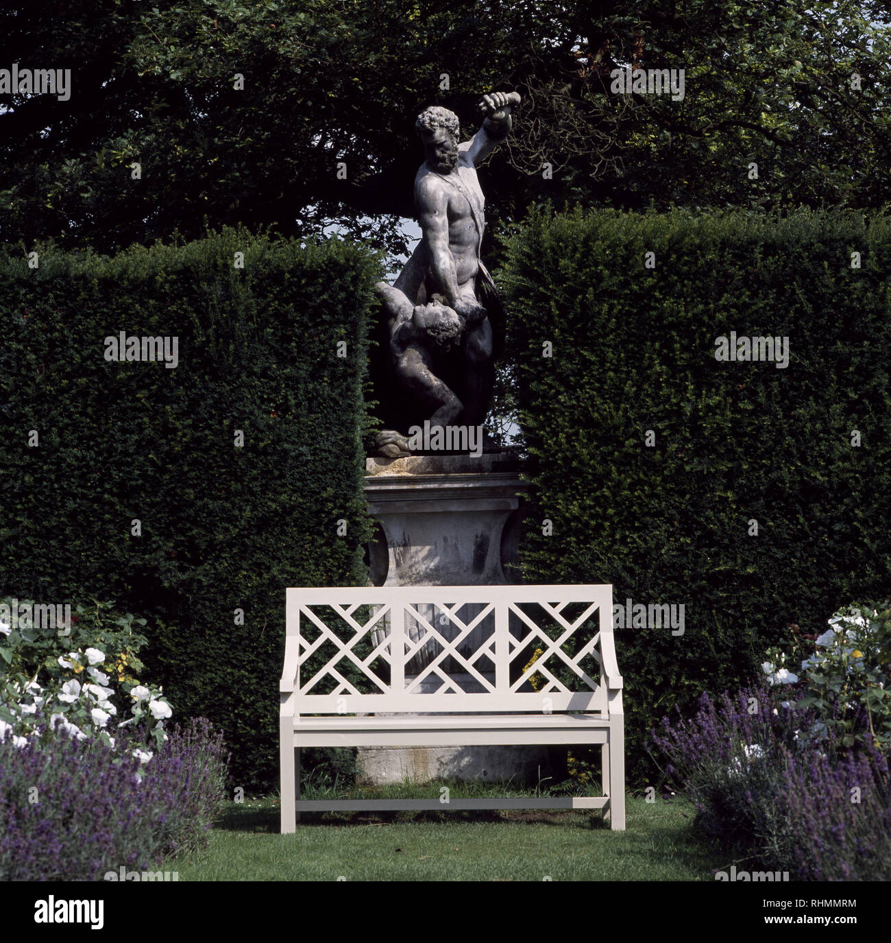 Clipped hedge and classical statue on plinth behind white seat Stock Photo