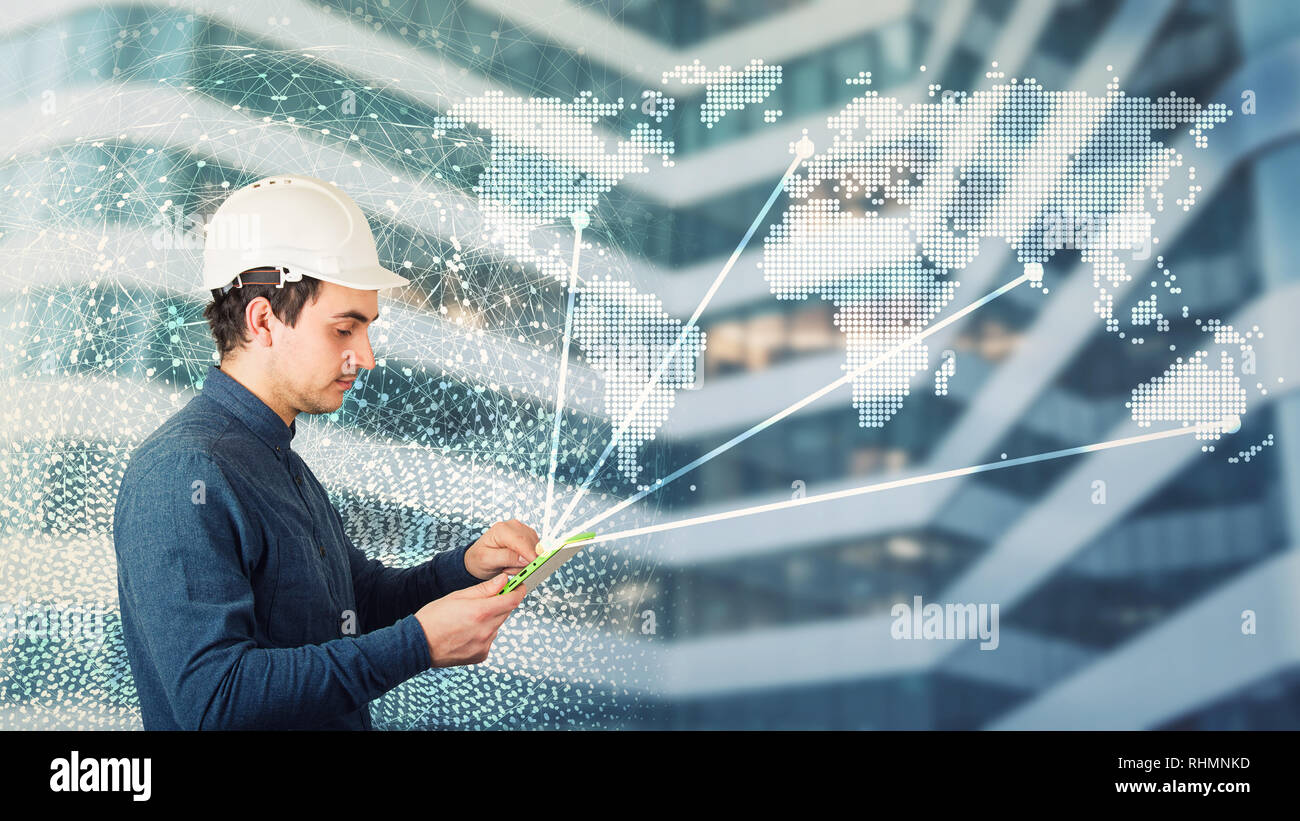 Side view man engineer wearing protective helmet using a tablet computer gadget choosing destinations on the world map. Modern technology artificial i Stock Photo