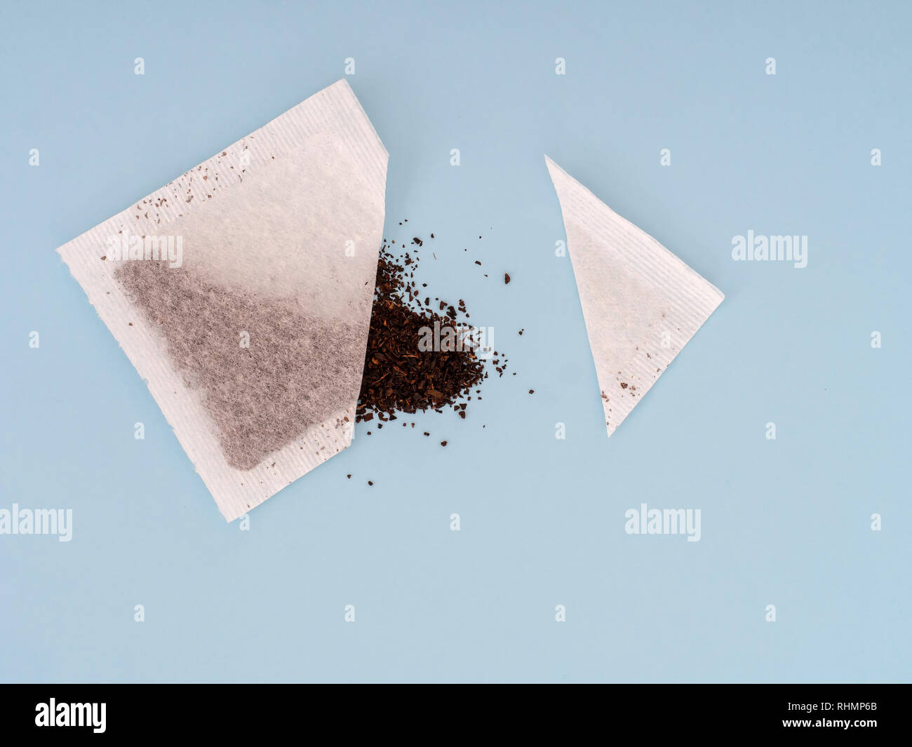 Tea bag sachet cut open to see contents and quality of leaves inside, on pale blue background. Stock Photo