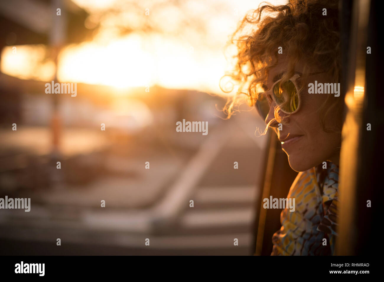 Beautiful sunny sunset time portrait for cute lady smiling and enjoying the feeling with the freedom outdoor - curly hair in the wind and sunglasses f Stock Photo