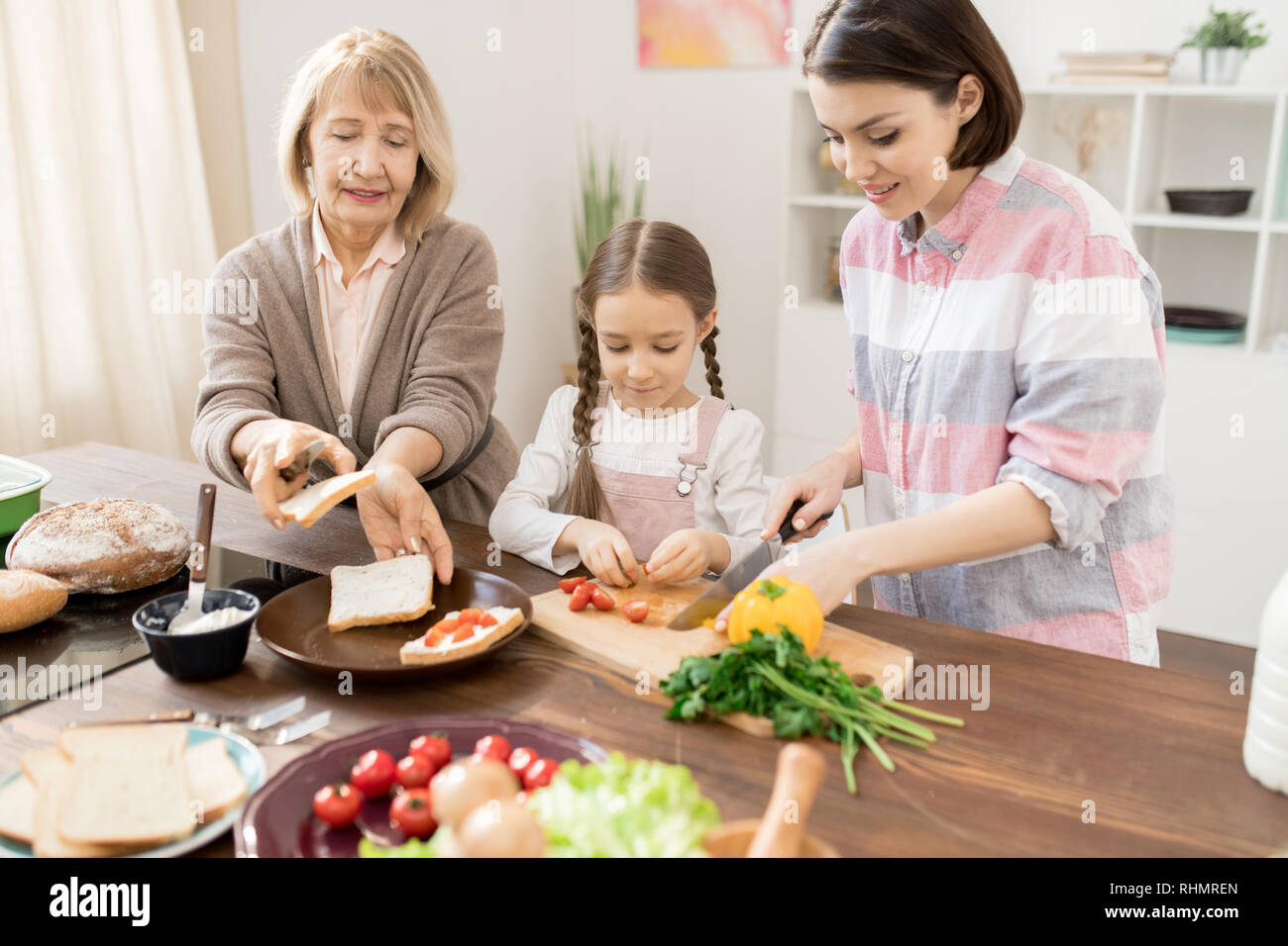 Young woman cutting tomatoes on board while her daughter and mother ...