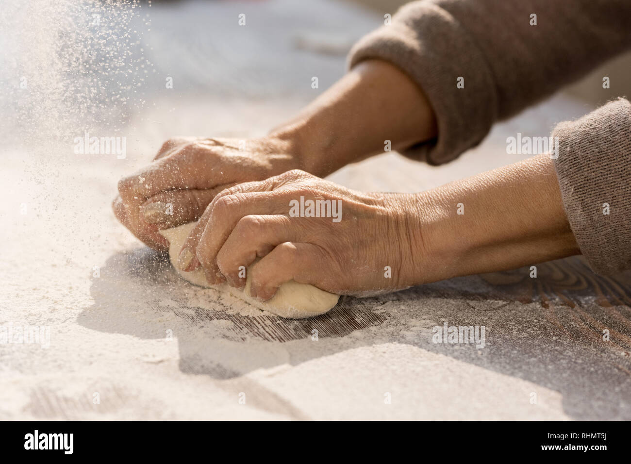 Hands of mature female kneading dough in flour on wooden table before ...