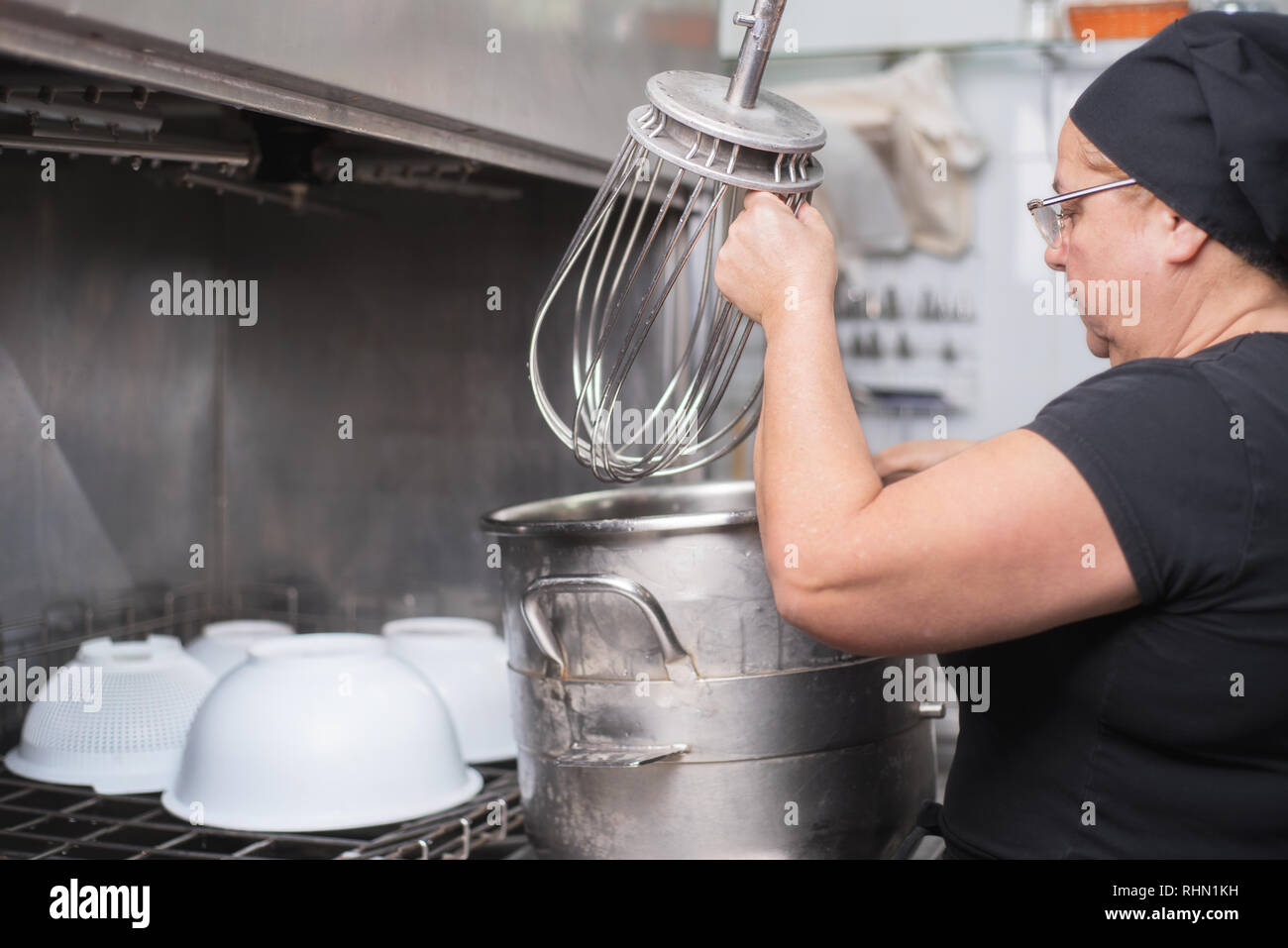 woman employee loading casseroles into an industrial dishwasher in the