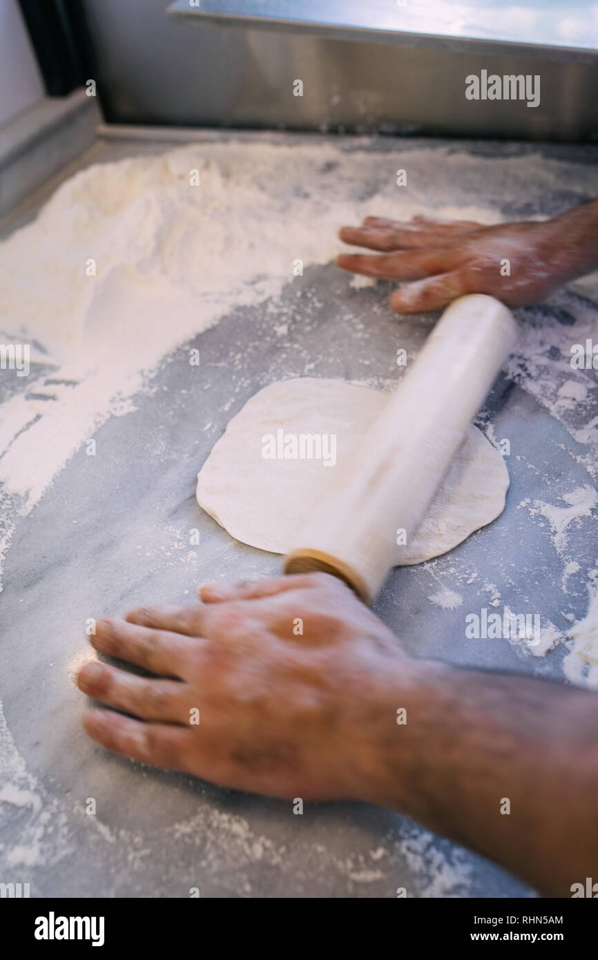 Hands kneading dough on table. Man hands keep rolling pin on dough with