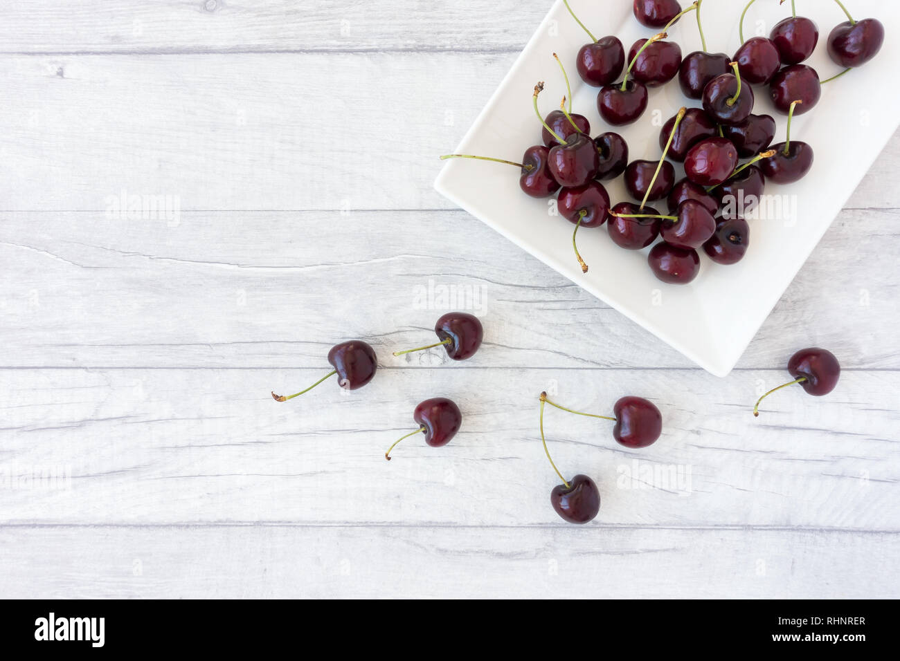 Cherries on a white plate and scattered on gray wood panel background. Top view and lots of copy space. Stock Photo